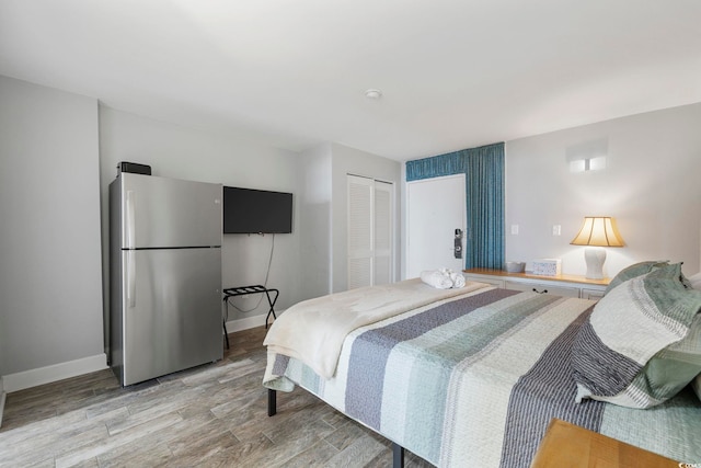 bedroom featuring wood-type flooring, stainless steel refrigerator, and a closet