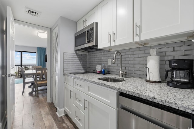 kitchen featuring sink, white cabinetry, stainless steel appliances, light stone counters, and decorative backsplash