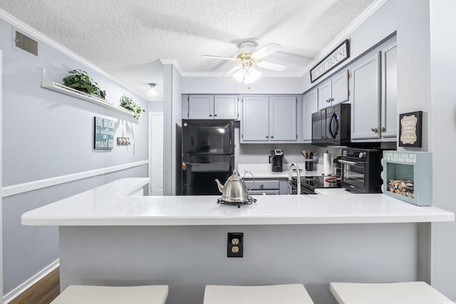 kitchen with kitchen peninsula, ornamental molding, black appliances, and a kitchen breakfast bar