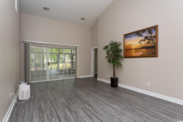 empty room featuring visible vents, baseboards, a high ceiling, and wood finished floors