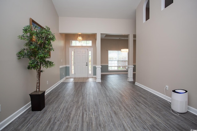 foyer entrance with a towering ceiling, baseboards, dark wood-style flooring, and ornate columns