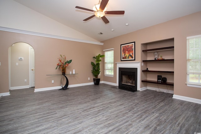 unfurnished living room featuring wood finished floors, baseboards, lofted ceiling, a fireplace with flush hearth, and arched walkways