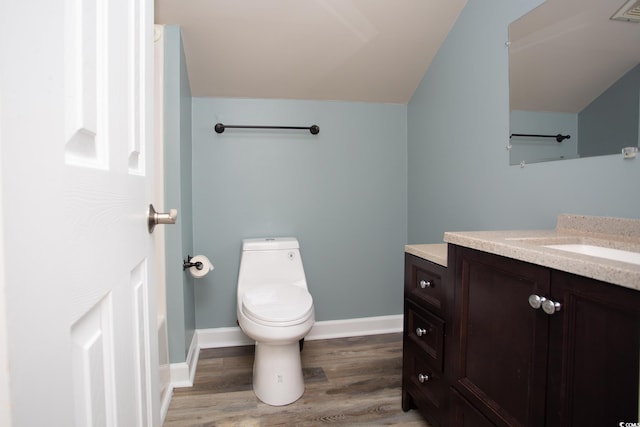 half bath featuring toilet, wood finished floors, baseboards, vanity, and vaulted ceiling