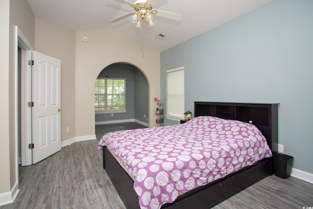 bedroom with visible vents, lofted ceiling, wood finished floors, arched walkways, and baseboards