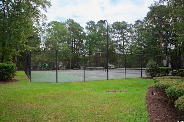 view of tennis court featuring fence and a lawn