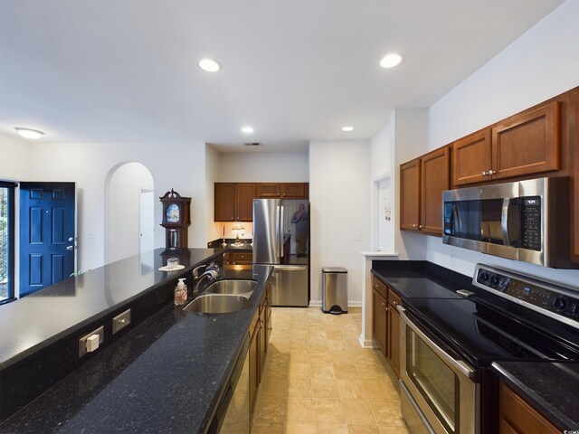 kitchen featuring appliances with stainless steel finishes, dark stone counters, sink, and light tile patterned floors