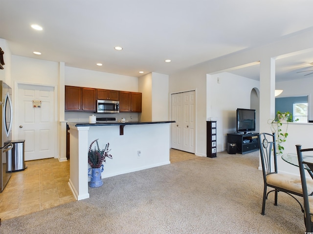 kitchen featuring ceiling fan, appliances with stainless steel finishes, light carpet, and a breakfast bar area