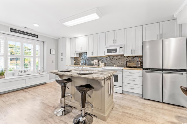 kitchen featuring white cabinetry, white appliances, a kitchen bar, light stone countertops, and a kitchen island