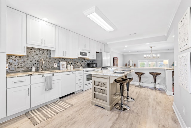 kitchen featuring white appliances, a breakfast bar, a center island, and white cabinets