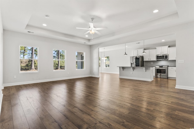 unfurnished living room with ceiling fan, dark hardwood / wood-style flooring, and a tray ceiling