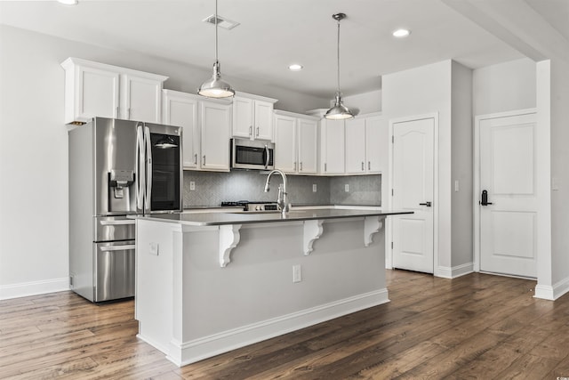 kitchen with stainless steel appliances, white cabinetry, a breakfast bar area, hanging light fixtures, and a center island with sink