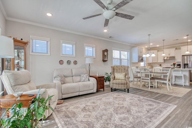 living room with ceiling fan with notable chandelier, crown molding, and light hardwood / wood-style flooring