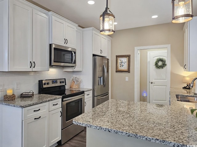 kitchen featuring stainless steel appliances, kitchen peninsula, pendant lighting, sink, and white cabinetry