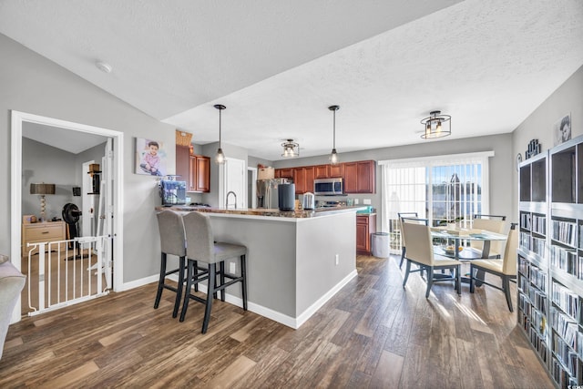 kitchen with kitchen peninsula, pendant lighting, dark hardwood / wood-style floors, stainless steel appliances, and a kitchen bar