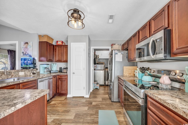 kitchen featuring sink, a textured ceiling, light wood-type flooring, a notable chandelier, and appliances with stainless steel finishes