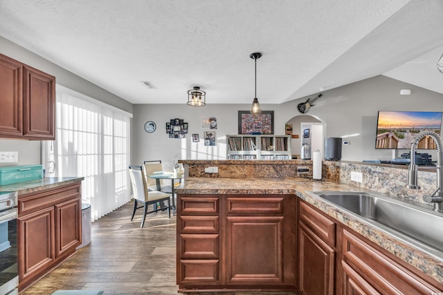 kitchen featuring a textured ceiling, dark wood-type flooring, sink, decorative light fixtures, and lofted ceiling