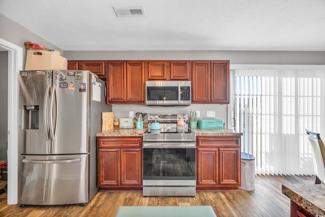 kitchen featuring a textured ceiling, stainless steel appliances, light stone countertops, and wood-type flooring