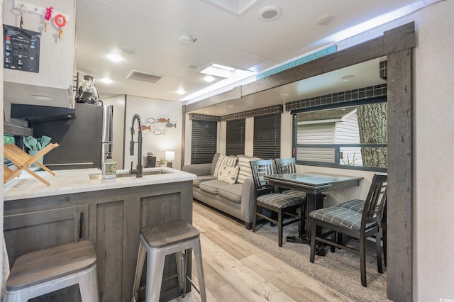 kitchen with sink, stainless steel fridge, a kitchen bar, and light hardwood / wood-style flooring