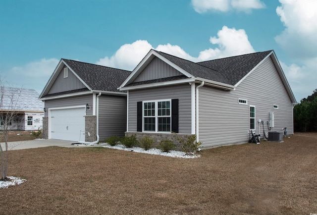 craftsman house with an attached garage, central air condition unit, driveway, roof with shingles, and a front yard