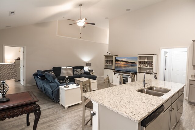 kitchen featuring stainless steel dishwasher, light hardwood / wood-style flooring, a center island with sink, gray cabinetry, and sink