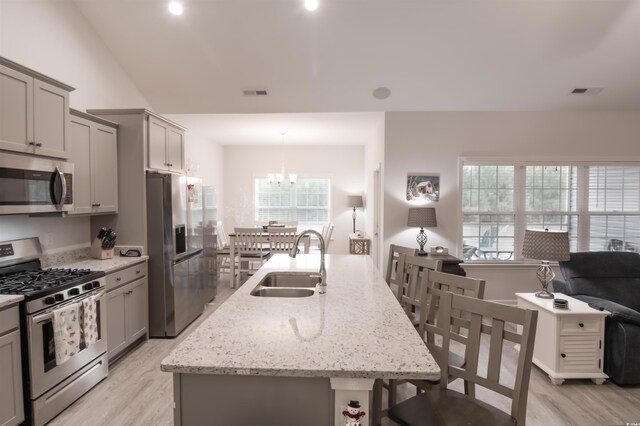 kitchen featuring sink, an island with sink, gray cabinetry, a notable chandelier, and appliances with stainless steel finishes