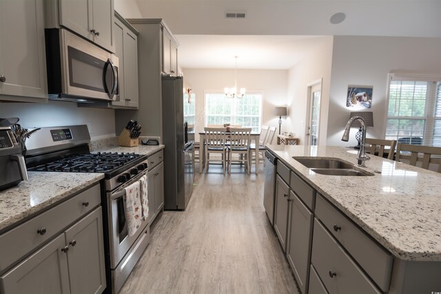 kitchen featuring gray cabinets, a center island with sink, stainless steel appliances, sink, and an inviting chandelier