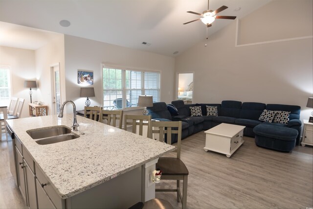 kitchen featuring light stone counters, light hardwood / wood-style flooring, a center island with sink, ceiling fan, and sink