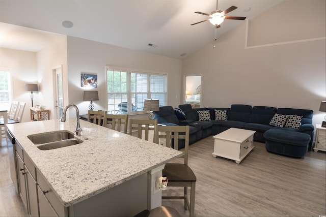 kitchen featuring an island with sink, sink, ceiling fan, light hardwood / wood-style floors, and light stone countertops