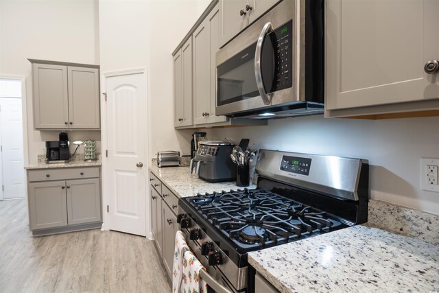 kitchen featuring light hardwood / wood-style floors, stainless steel appliances, light stone counters, and gray cabinets