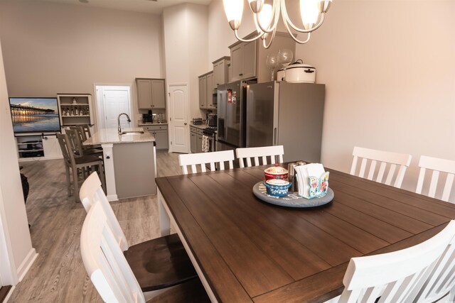 dining room featuring a towering ceiling, a notable chandelier, light hardwood / wood-style floors, and sink