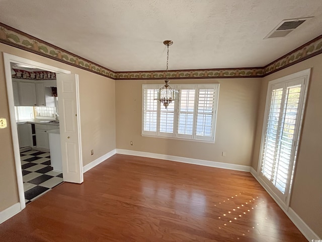 unfurnished dining area with visible vents, baseboards, wood finished floors, and an inviting chandelier