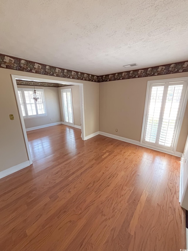 spare room with a textured ceiling, visible vents, baseboards, a notable chandelier, and light wood-style flooring