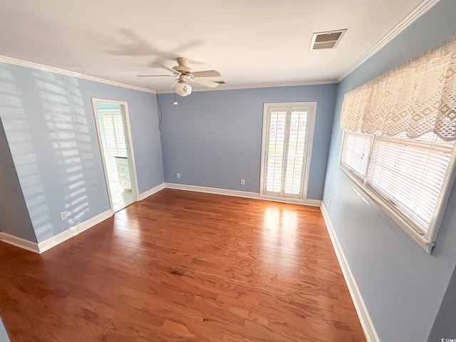 spare room featuring a ceiling fan, visible vents, crown molding, wood finished floors, and baseboards