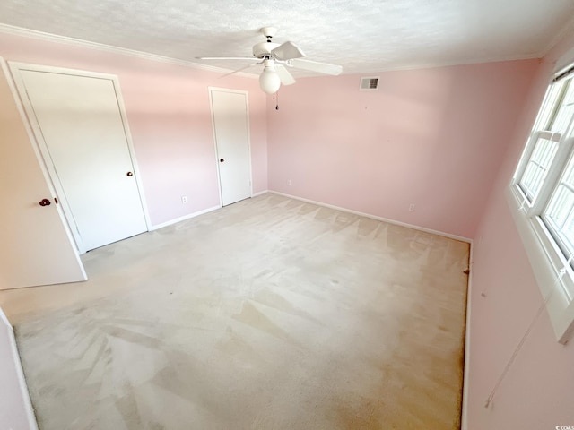 unfurnished bedroom with crown molding, light colored carpet, a textured ceiling, baseboards, and visible vents