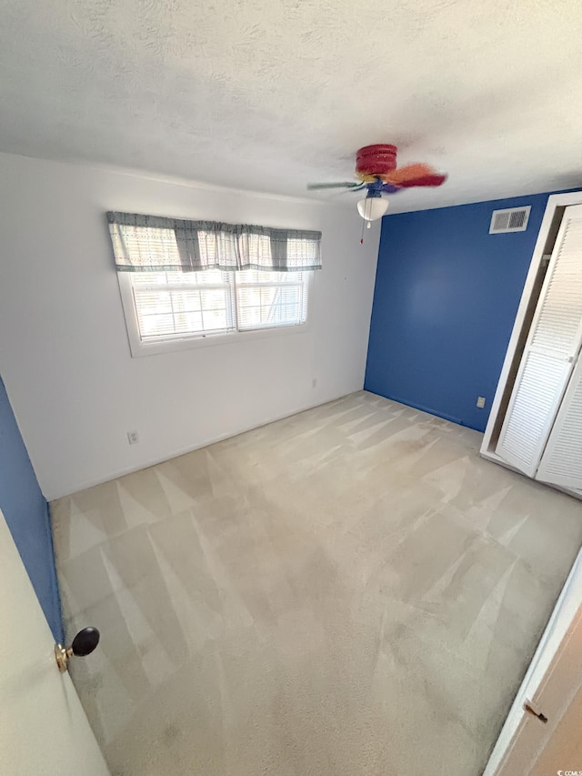 spare room featuring light colored carpet, ceiling fan, visible vents, and a textured ceiling