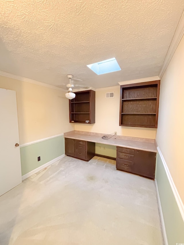unfurnished office with a textured ceiling, visible vents, a skylight, built in desk, and ornamental molding