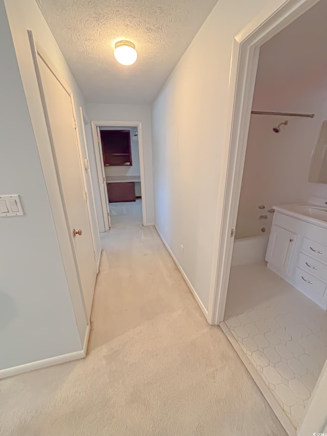 hallway with baseboards, light carpet, and a textured ceiling
