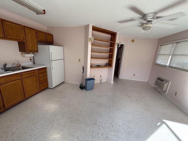 kitchen featuring brown cabinetry, a ceiling fan, a wall mounted AC, a sink, and freestanding refrigerator