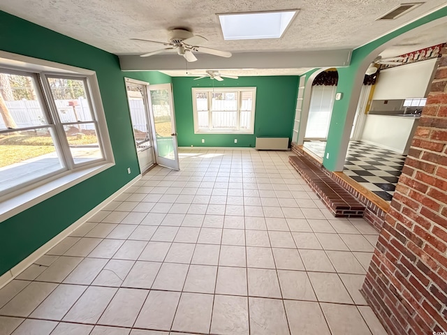 empty room featuring ceiling fan, arched walkways, a textured ceiling, a skylight, and visible vents
