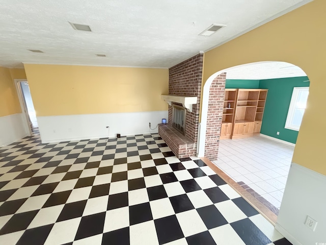 interior space featuring a textured ceiling, visible vents, arched walkways, a brick fireplace, and tile patterned floors