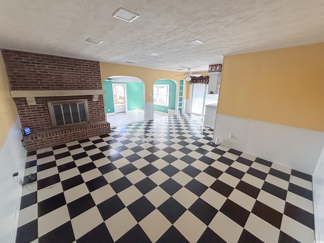 unfurnished living room featuring a brick fireplace, arched walkways, ceiling fan, and light floors