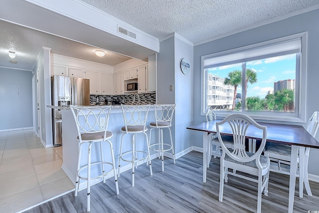 kitchen with crown molding, tasteful backsplash, visible vents, a peninsula, and stainless steel fridge with ice dispenser