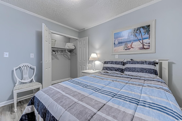 bedroom with a closet, ornamental molding, a textured ceiling, wood finished floors, and baseboards