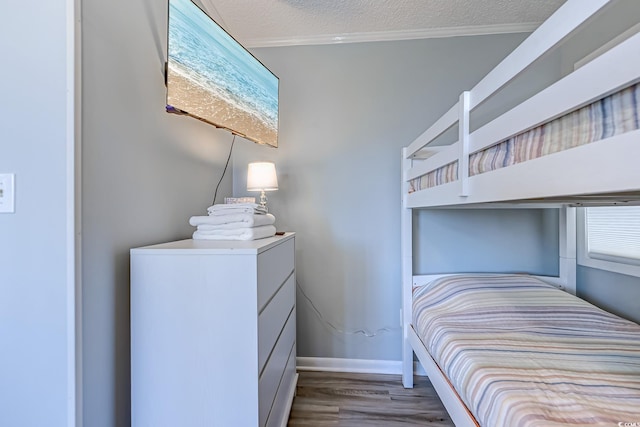 bedroom featuring crown molding, a textured ceiling, baseboards, and wood finished floors