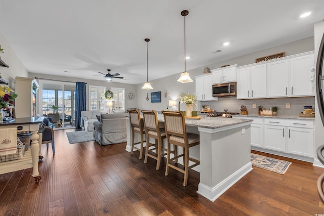 kitchen featuring decorative light fixtures, stainless steel microwave, open floor plan, white cabinets, and light stone countertops