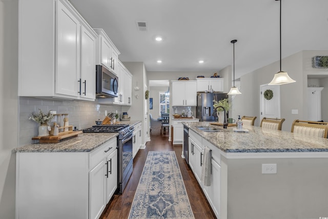 kitchen featuring visible vents, hanging light fixtures, stainless steel appliances, white cabinetry, and a sink