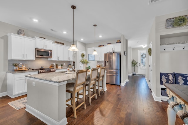 kitchen featuring appliances with stainless steel finishes, pendant lighting, white cabinetry, and an island with sink