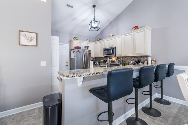 kitchen featuring lofted ceiling, backsplash, stainless steel appliances, light stone counters, and kitchen peninsula