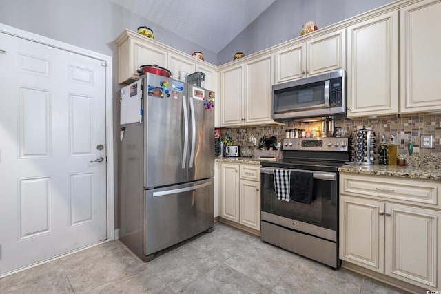 kitchen with stainless steel appliances, vaulted ceiling, cream cabinets, and decorative backsplash