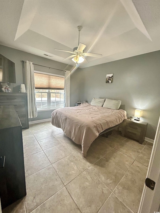 tiled bedroom with ceiling fan and a raised ceiling